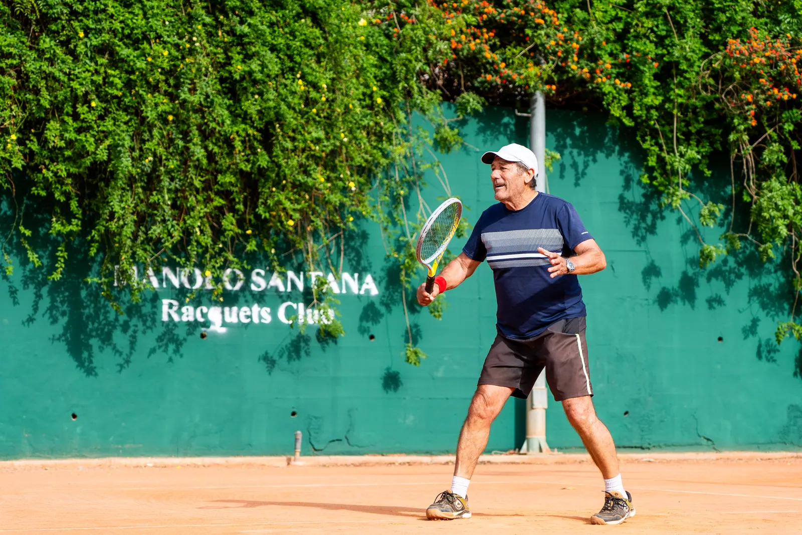Adult student playing on a clay court next to the club wall