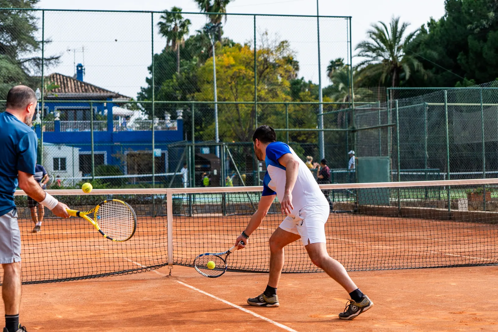 Adults playing at the net on a clay court